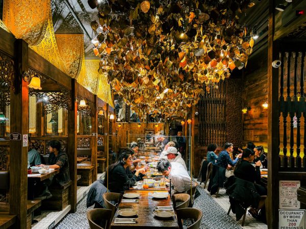 The indoor seating area of a restaurant with rows of tables, chairs and booths and gold-leaf chandeliers.