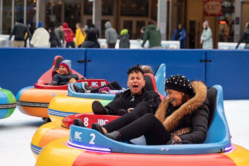 Kids and adults are using the colorful ice bumper cars in Bryant Park. A person exclaims in delight while others around her laugh and smile.