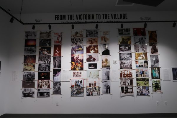 A white wall with many photographs of black artists. The title of the show “From The Victoria to The Village” is written above the images.