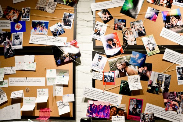 Four corkboards with photographs and written and printed notes pinned on them. Some notes and photographs and linked by white strings.