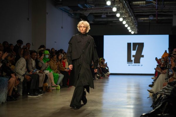 A model walking down a runway in a tiered black button-down and black pants.