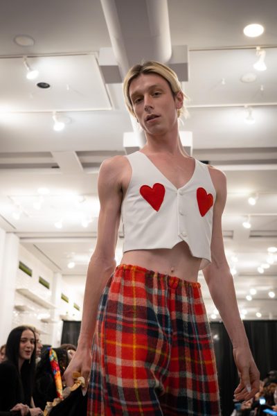 A model poses with a white waistcoat with red hearts and red plaid pants.