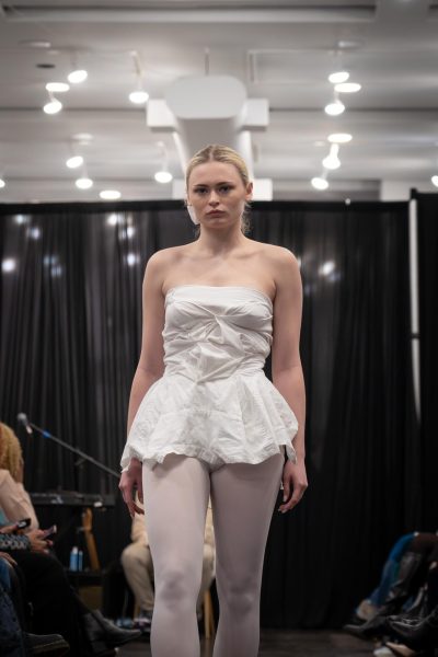 A model walks down a runway in sheer white tights and a strapless white top.