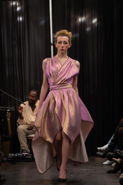A model walks down a runway in a glittery champagne dress with petal-like layers.