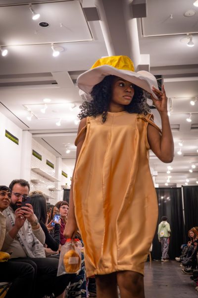 A model poses on a runway wearing a silk dress and a white hat.