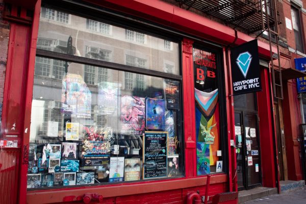A red storefront with a sign that says “WAYPOINT CAFE N.Y.C.” above its entrance. Numerous posters and toys are showcased in its window.