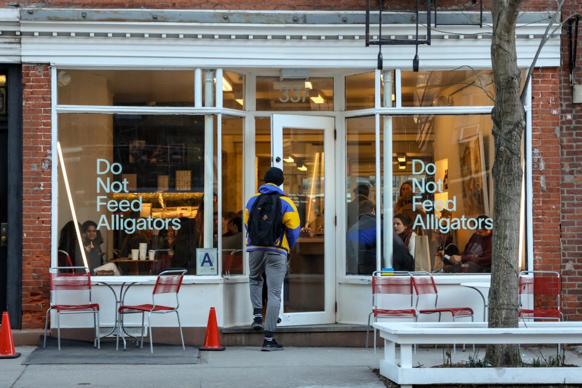 A customer walks into a white storefront with glass windows that say “Do Not Feed Alligators.” Red chairs are placed outside the storefront.