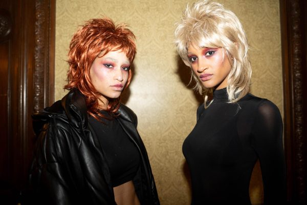Two models with pink eyeshadow look into the camera. One is wearing a ginger wig, the other a blonde wig.