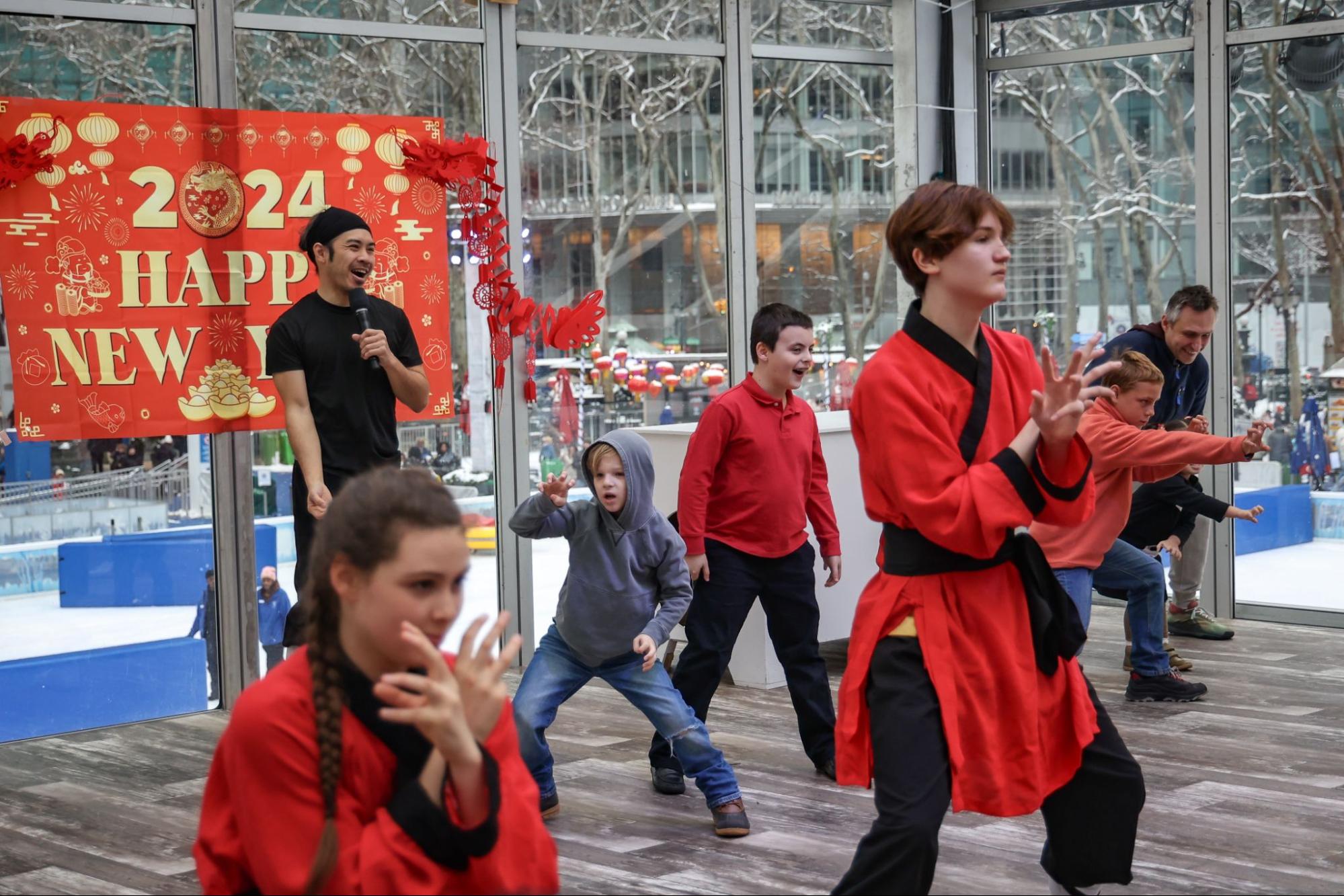 A group of people wearing red and black outfits doing Chinese martial arts in a room.
