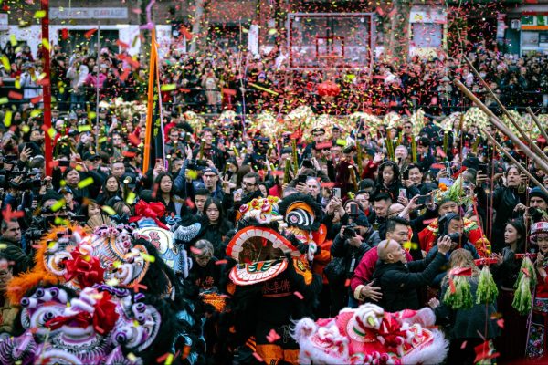 A large crowd filled by lion dancers and other people standing while red and yellow confetti is falling.