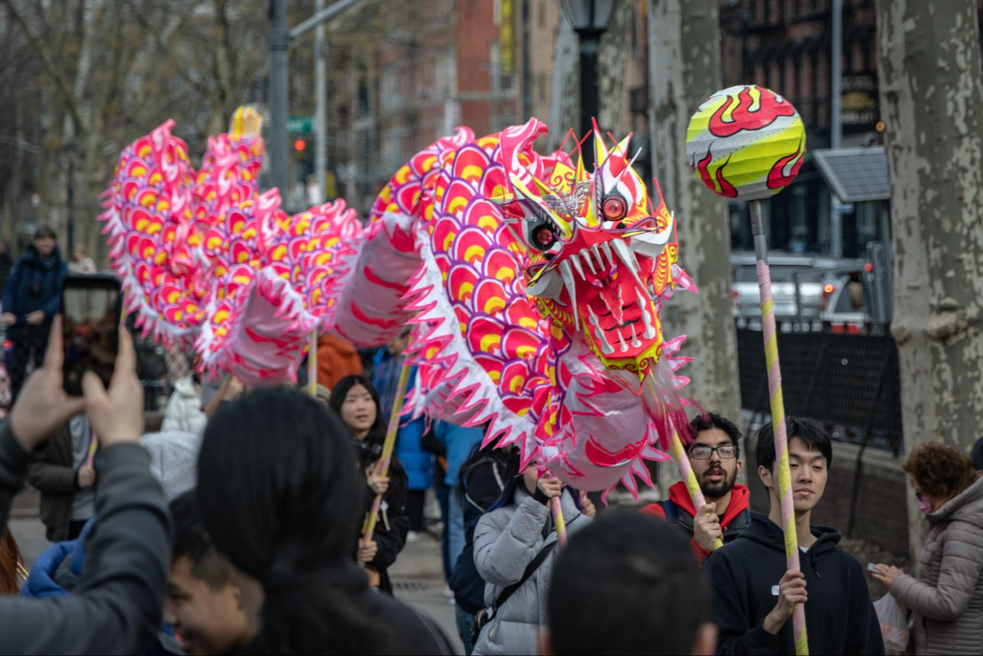 A red and yellow dragon held by a group of people marching down a street in a parade.