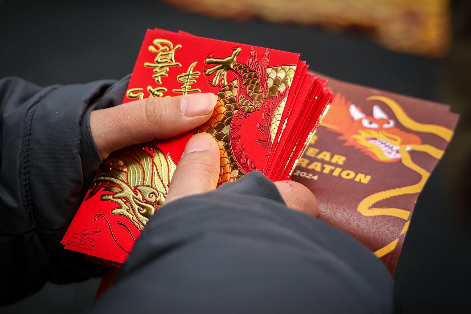A close-up shot of a person’s hands holding red envelopes with dragon designs.