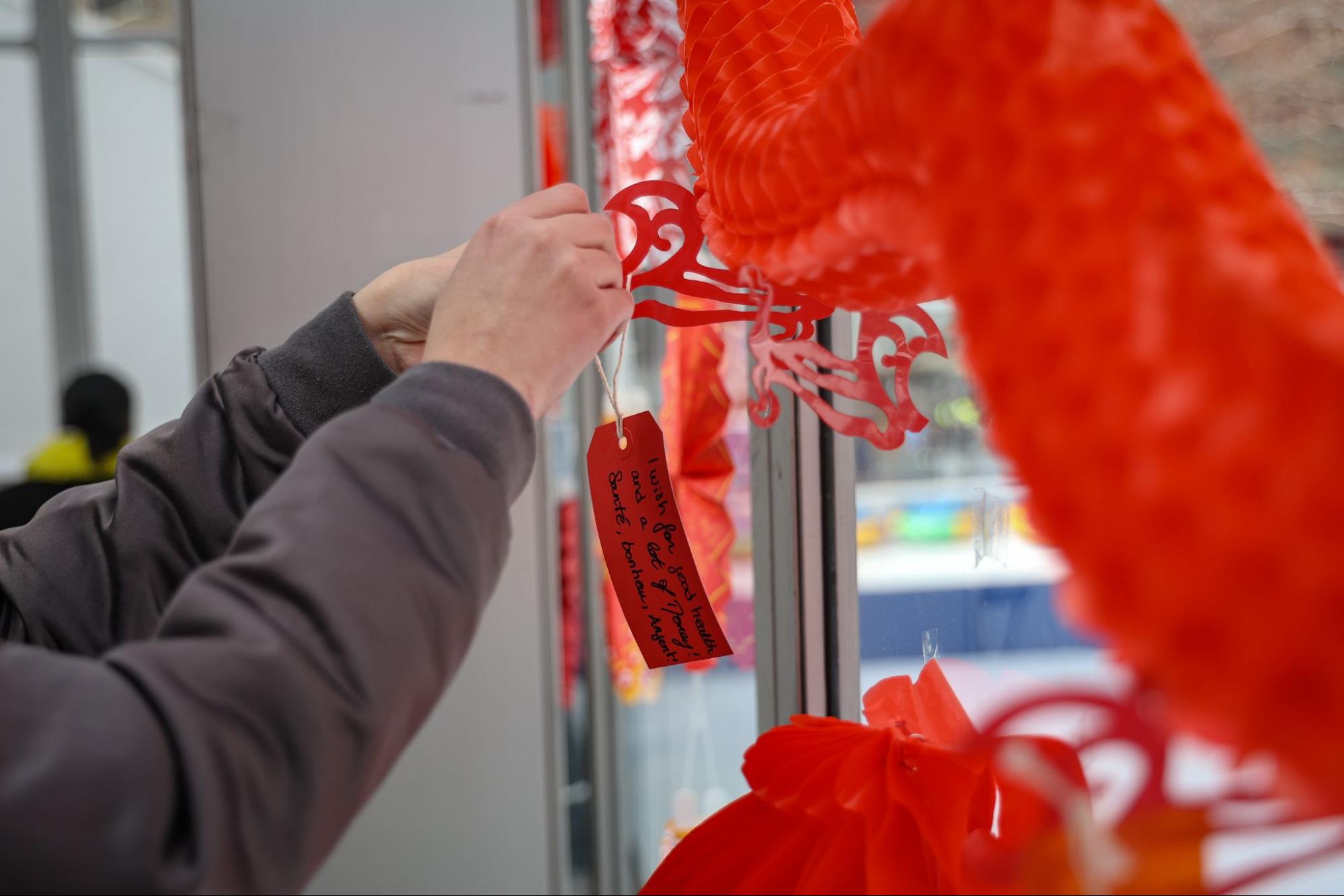 A person ties a red tag with a wish for the New Year onto a window with red decoration.