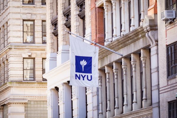A white flag with a purple N.Y.U. logo at its center is placed on a building.