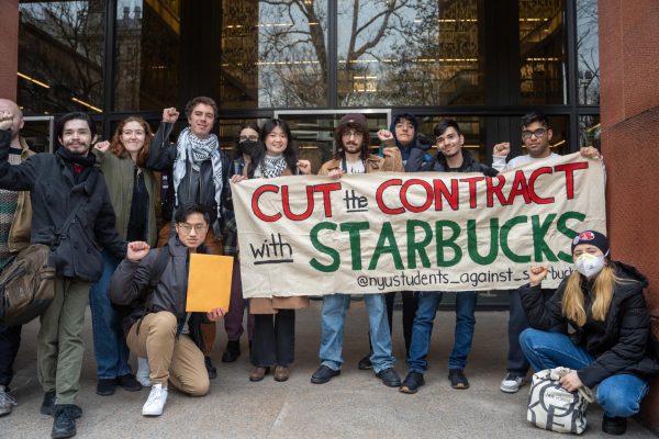 A group of students posing for a group photo in front of N.Y.U.’s Bobst Library. Some students on the right are holding a white banner with the red, green and red words “CUT the CONTRACT with STARBUCKS” written on it. A student beside the banner is holding a yellow envelope.