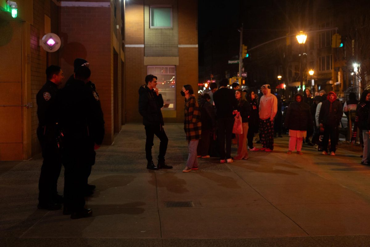 A crowd of students and three police officers stand outside Alumni Hall.