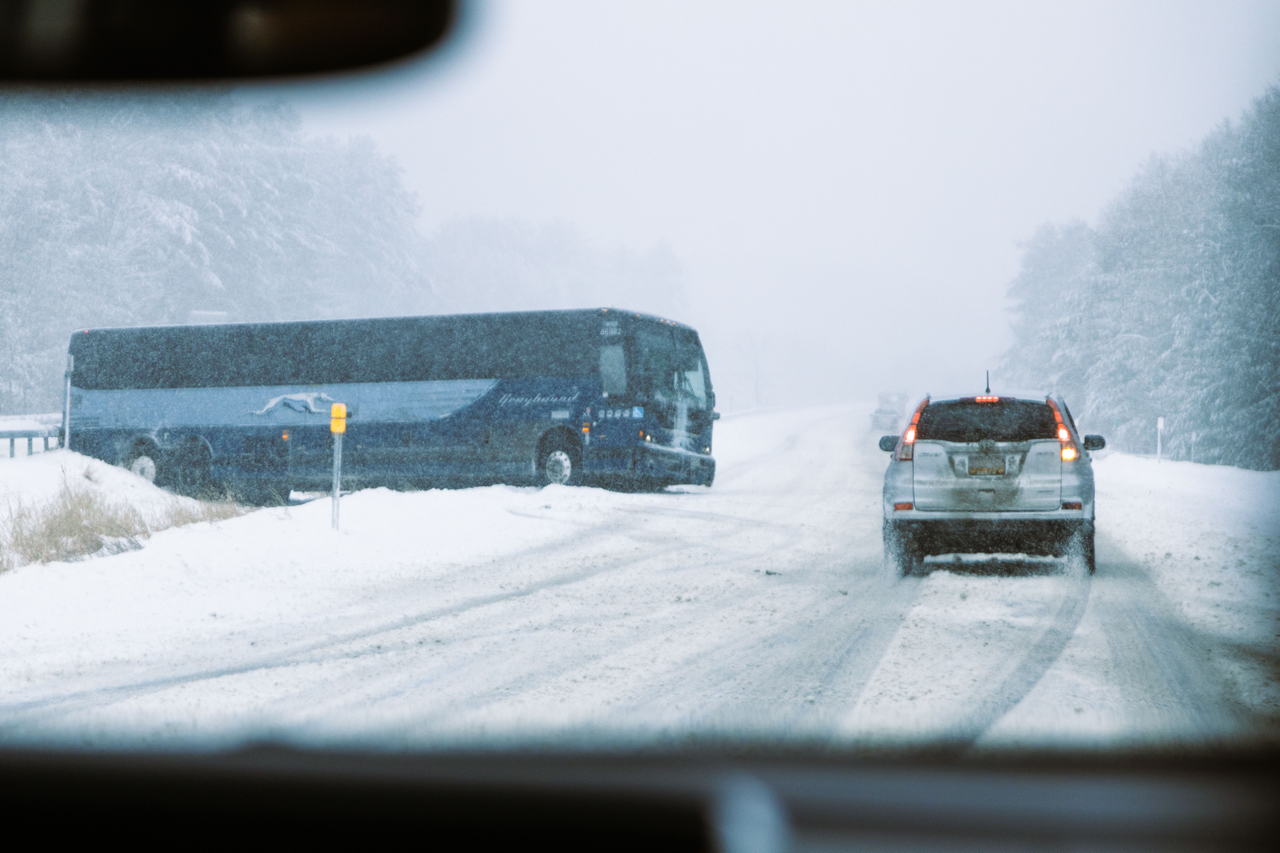 A snowy road lined with cars and a Greyhound bus crashed into a guard rail.