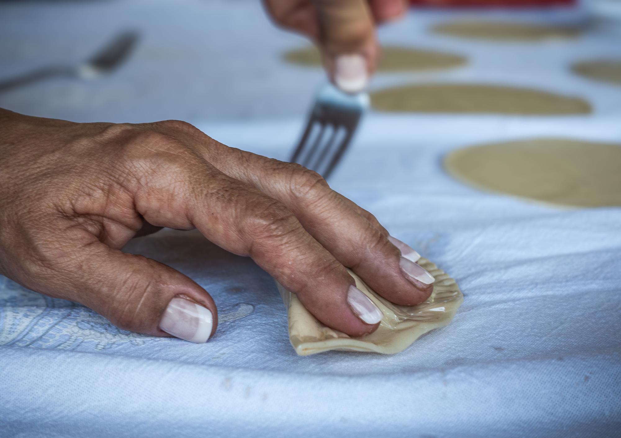 A person holding down a pastel with one hand while using a fork to press down the edges with their other hand.