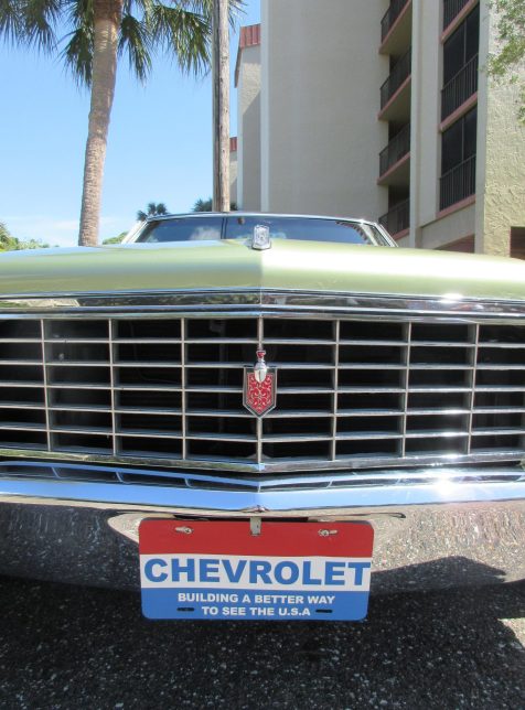 The front bumper of a green Chevrolet with a sign on the license plate that reads “CHEVROLET BUILDING A BETTER WAY TO SEE THE U.S.A.”