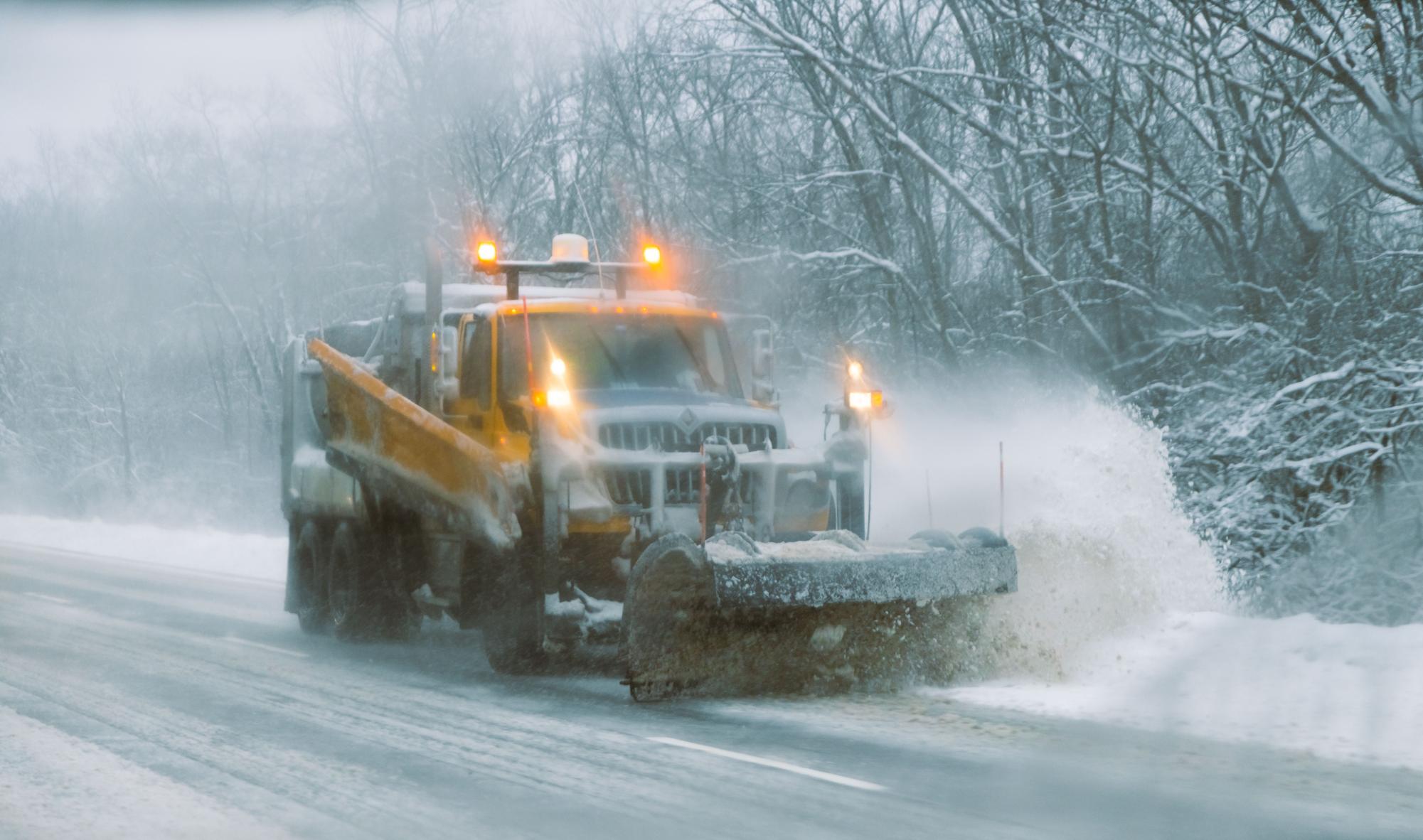 A snow plow truck plowing snow on a road.