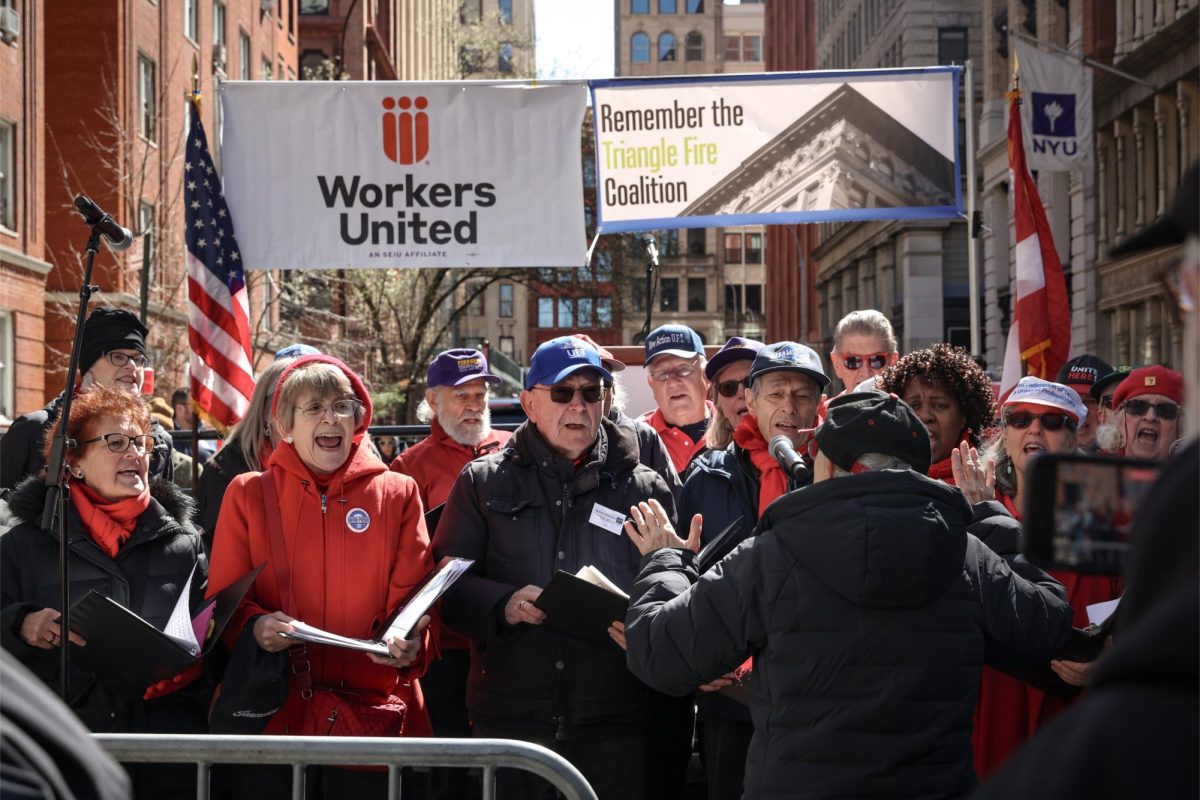 A choir in various black and red garments perform under banners reading, “Workers United” and “Remember the Triangle Fire Coalition.”