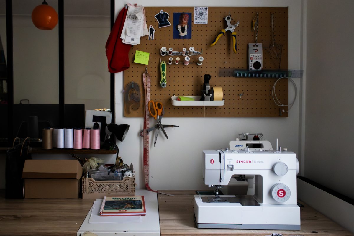 A+sewing+machine+on+a+desk+with+a+peg+board+of+other+tools+hanging+above+it.