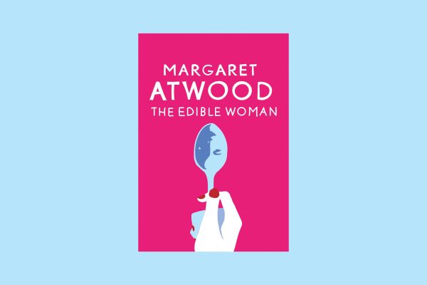 Hot pink book cover on a light blue background with the words "THE EDIBLE WOMAN" and "MARGARET ATWOOD" in white font. A hand with red polished nails holds a spoon which reflects a woman's face.