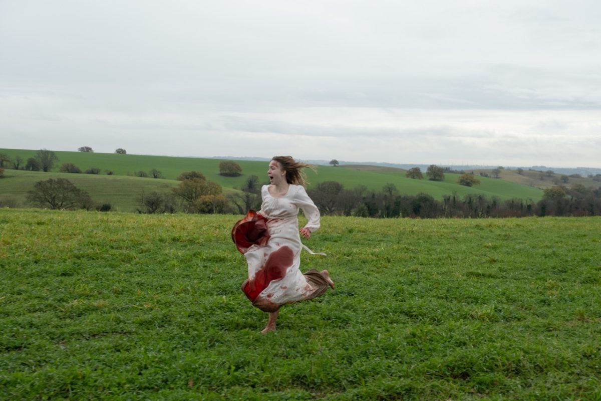 A photograph of a screaming woman running through a green, empty field in a white blood-stained dress.
