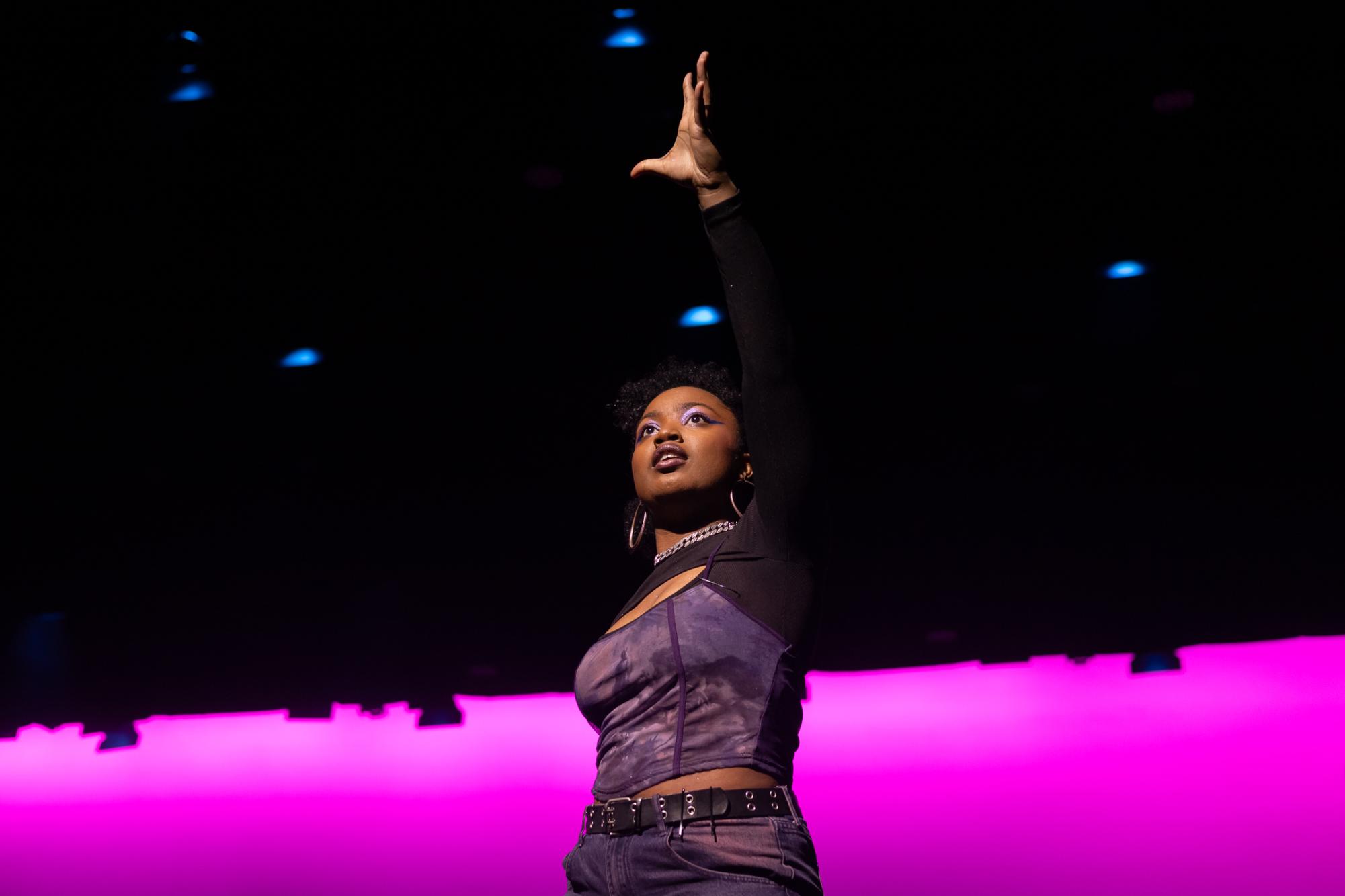 A woman reaches her hand upward toward a crowd while onstage.