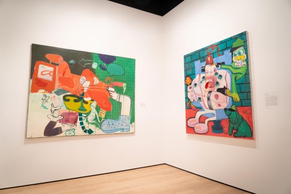 Two abstract paintings are hung on two walls in a corner inside an art gallery.