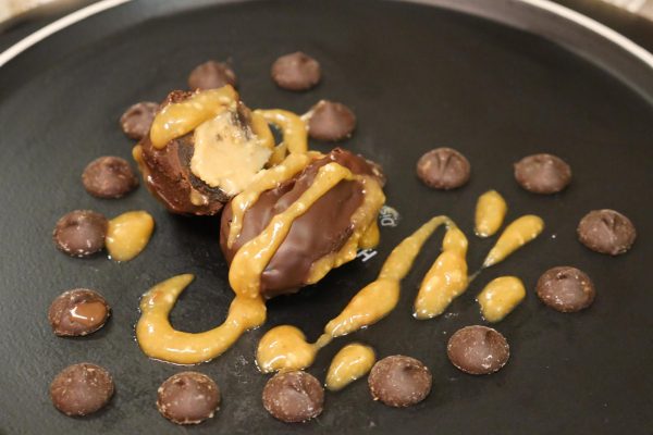 Dates covered in peanut butter, peanuts and chocolate plated on a with chocolate garnish in a heart shape.
