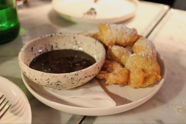 Fried zeppoles with powdered sugar on top next to a bowl of chocolate.