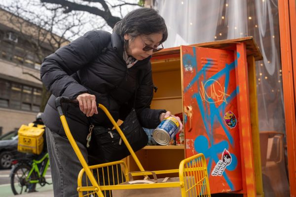 A woman grabs a can from an orange locker and places it in her cart.