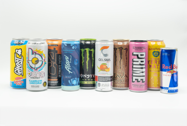 Line of colorful tin cans arranged next to each other. From left to right: “GHOST” on a yellow and blue can, “BANG ENERGY” on a white and blue can , “C4” on a black and orange can, “ALANI NU” on a blue and mint green can, “MONSTER” on a black and neon green can, “CELSIUS” on an orange and white can, “JAVA MONSTER” on a brown can, “PRIME” on a pink and white can, “YERBA MATE” on a yellow and red can and “RED BULL” on a blue and tin can.