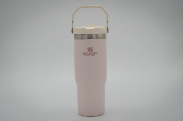 A light pink water bottle with a white lid and a white handle, with “STANLEY” written on it, against a white background.
