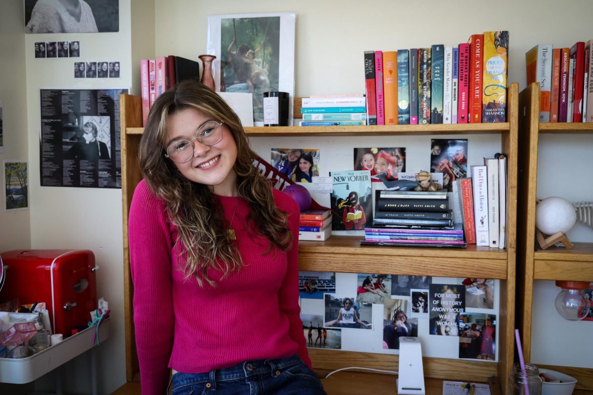 A girl sitting on a dormitory desk decorated with pictures and books.