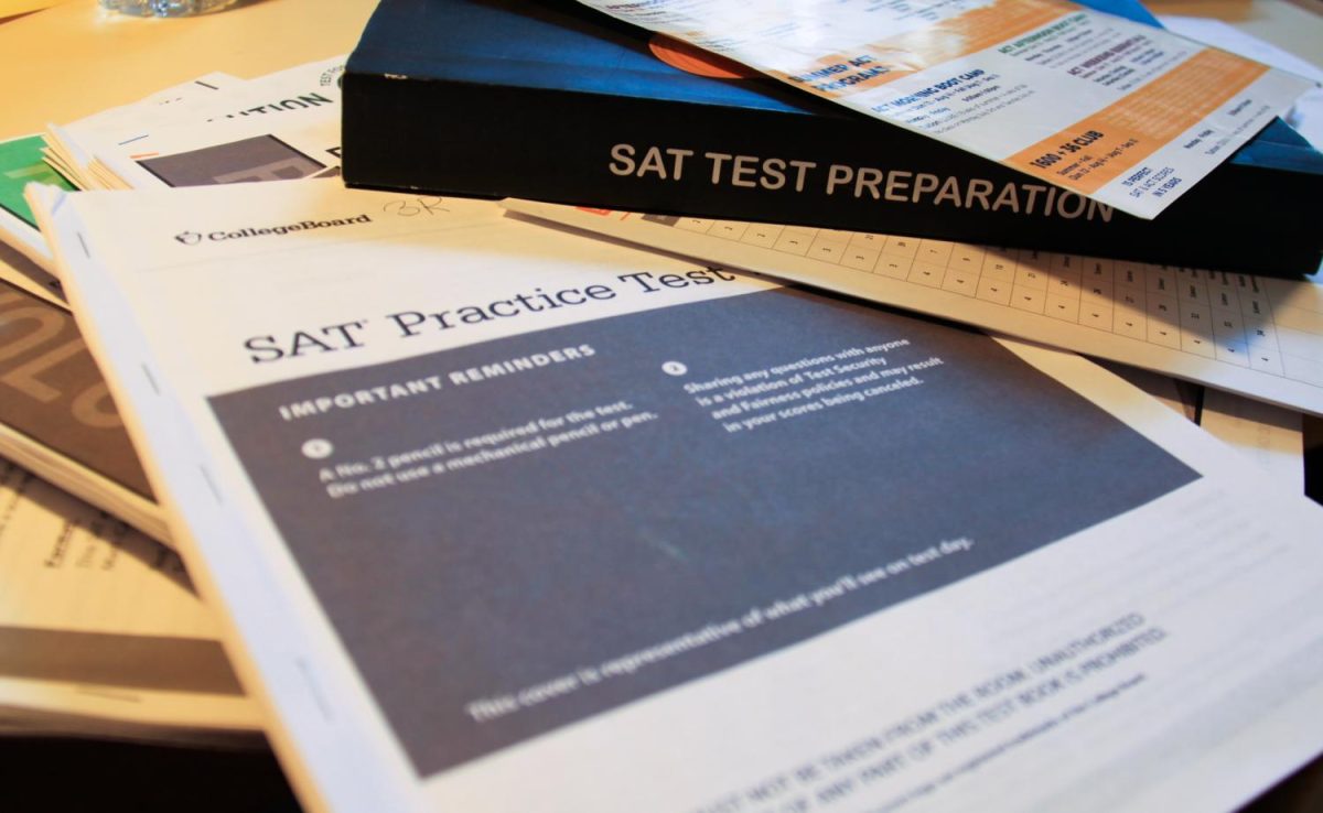 An S.A.T. a practice pamphlet sits alongside a book featuring the words "S.A.T. Test Preparation" on it, and other study items on a desk.