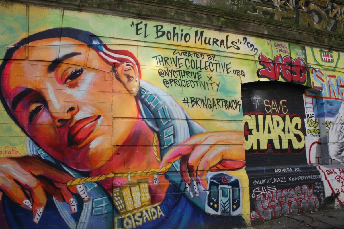 A mural of a woman’s face holding up a chain with the word “LOISAIDA” and a gold cityscape. The words “el bohio murals” and “#BRINGARTBACK” are next to the woman alongside the words “CURATED BY … THRIVECOLLECTIVE.ORG.”