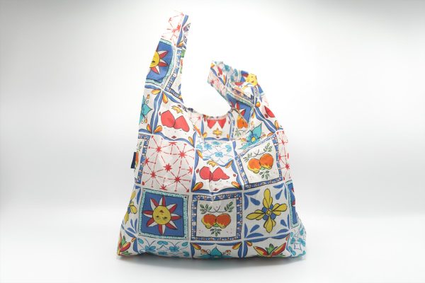 Reusable grocery bag tote with a blue, white and red tile pattern, along with drawings of the sun and various fruits.
