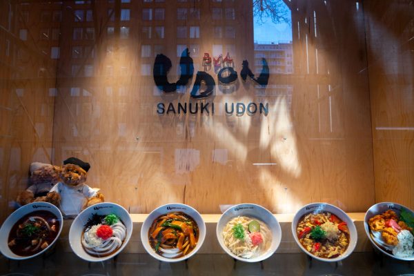 Six bowls of food and two teddy bears wearing chef outfits sit inside the storefront window of “Sanuki Udon.”