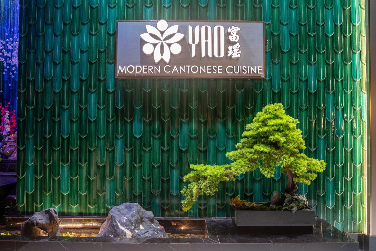 Sign saying “YAO MODERN CANTONESE CUISINE” on a green, tiled wall. Under the sign are a bonsai tree and a small pool of water with rocks.