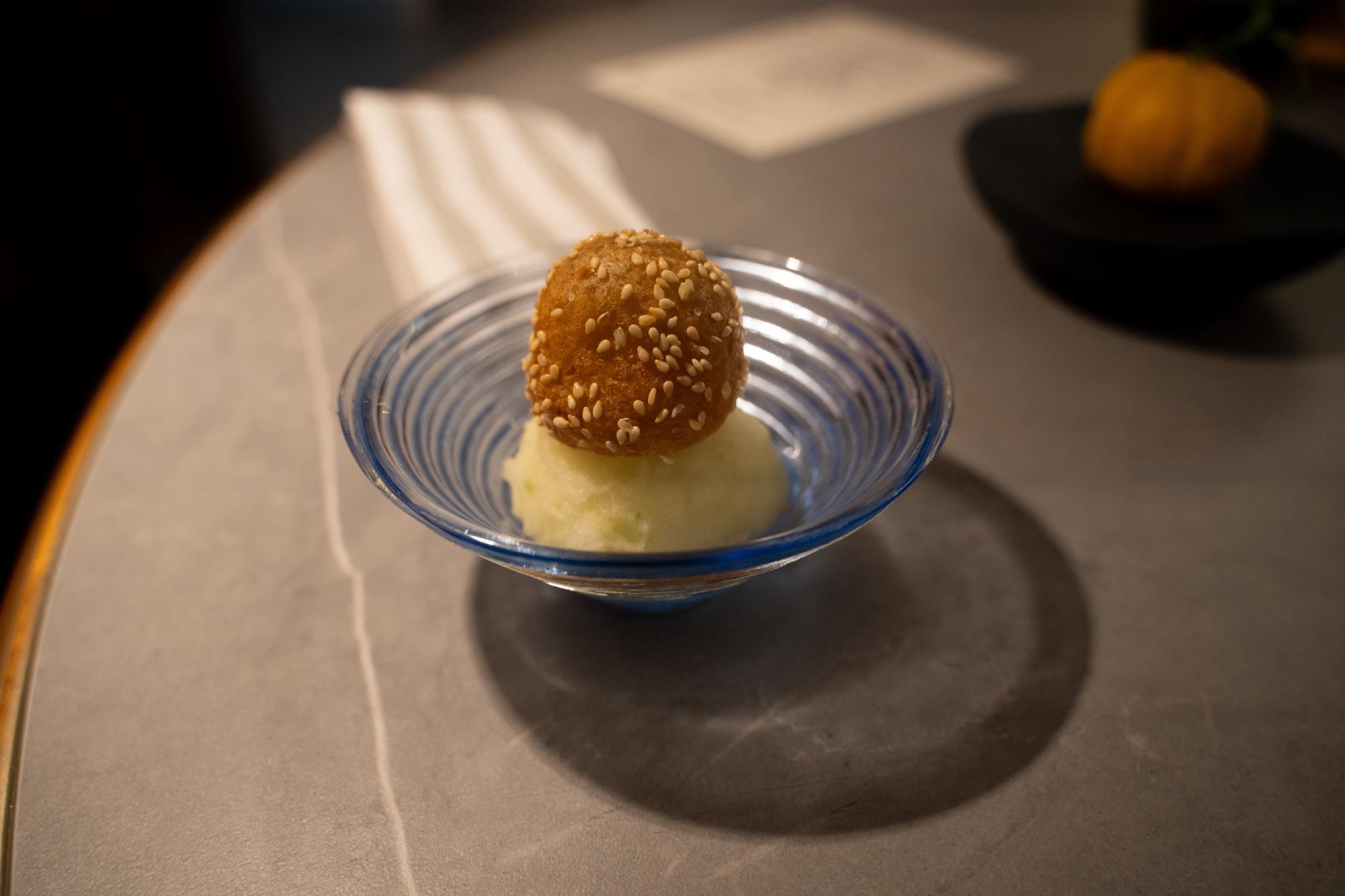 Small blue dish with a sesame ball on top of apple sorbet.