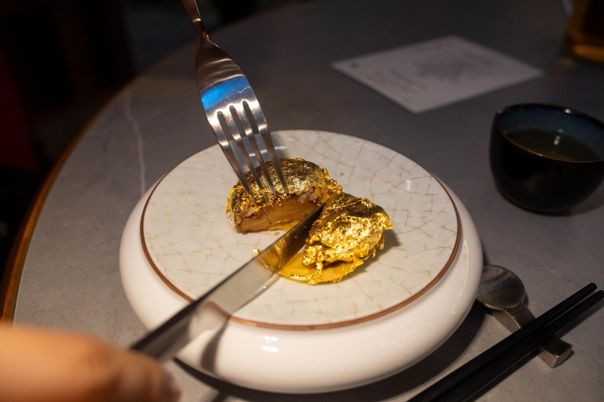 A knife and fork cut into a piece of gold leaf wrapped abalone.