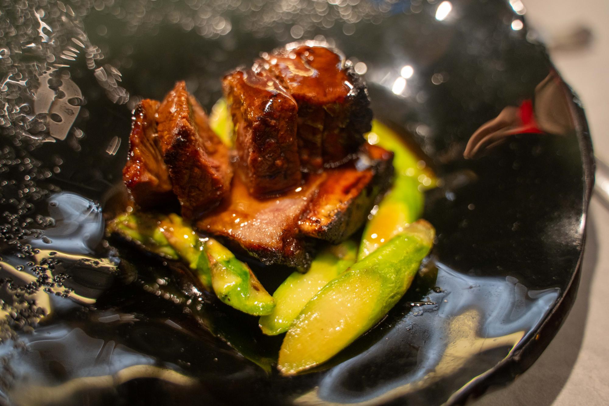 Sliced short ribs covered in sauce on top of avocado slices.