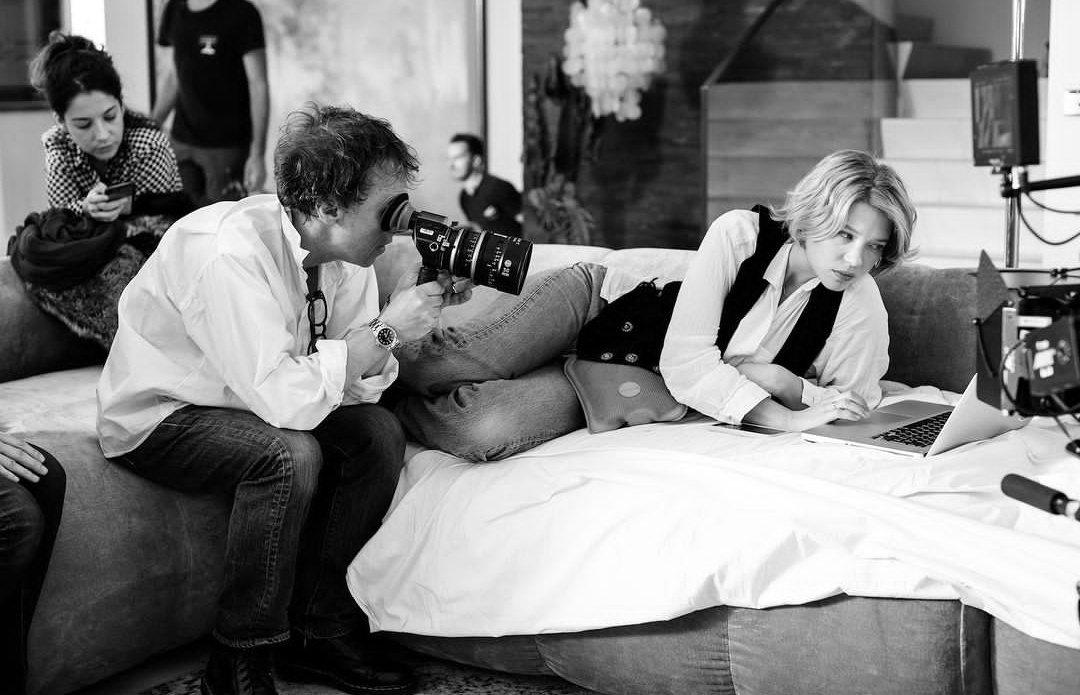 Black and white photo of people on a couch. A man is holding a video camera while the woman next to him looks at a computer.