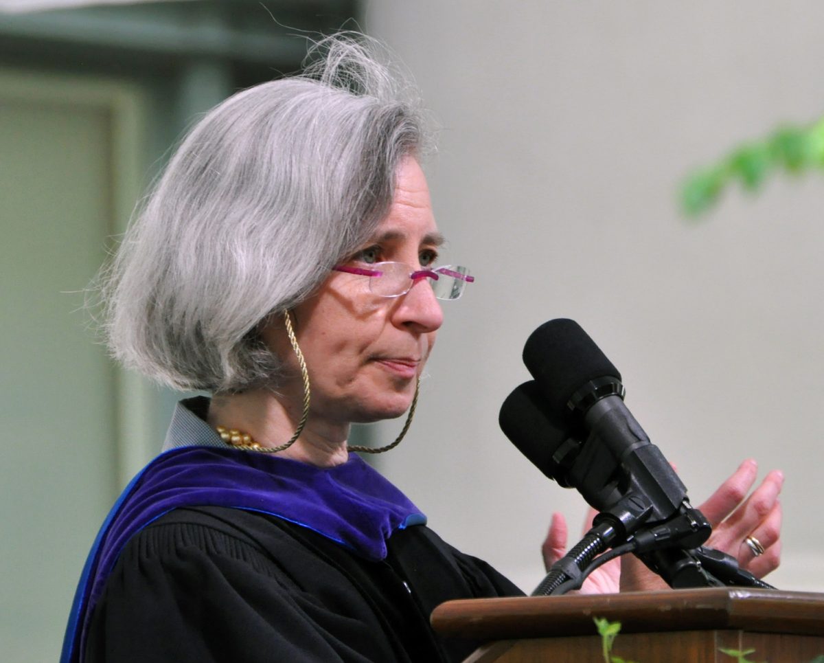 A woman standing by a podium in graduation regalia.