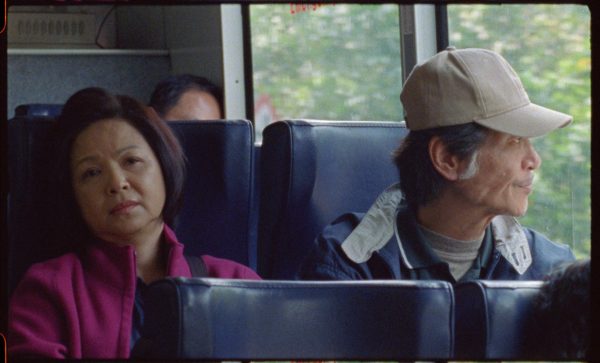 Two people sitting on a bus. The woman is staring ahead and the man is wearing a hat and staring out the window.