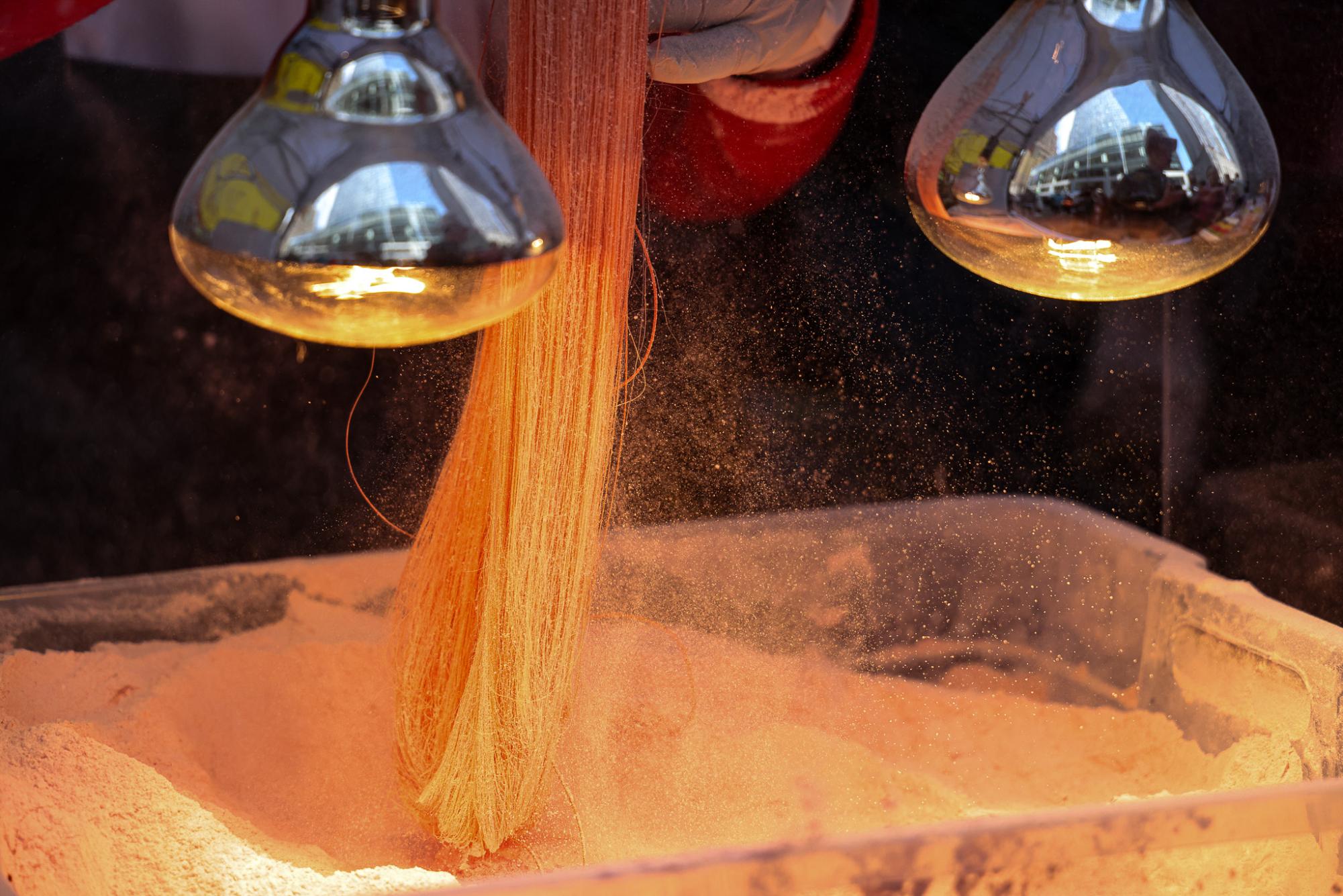 A person pulling thin strands of candy in sugar at a festival food station.