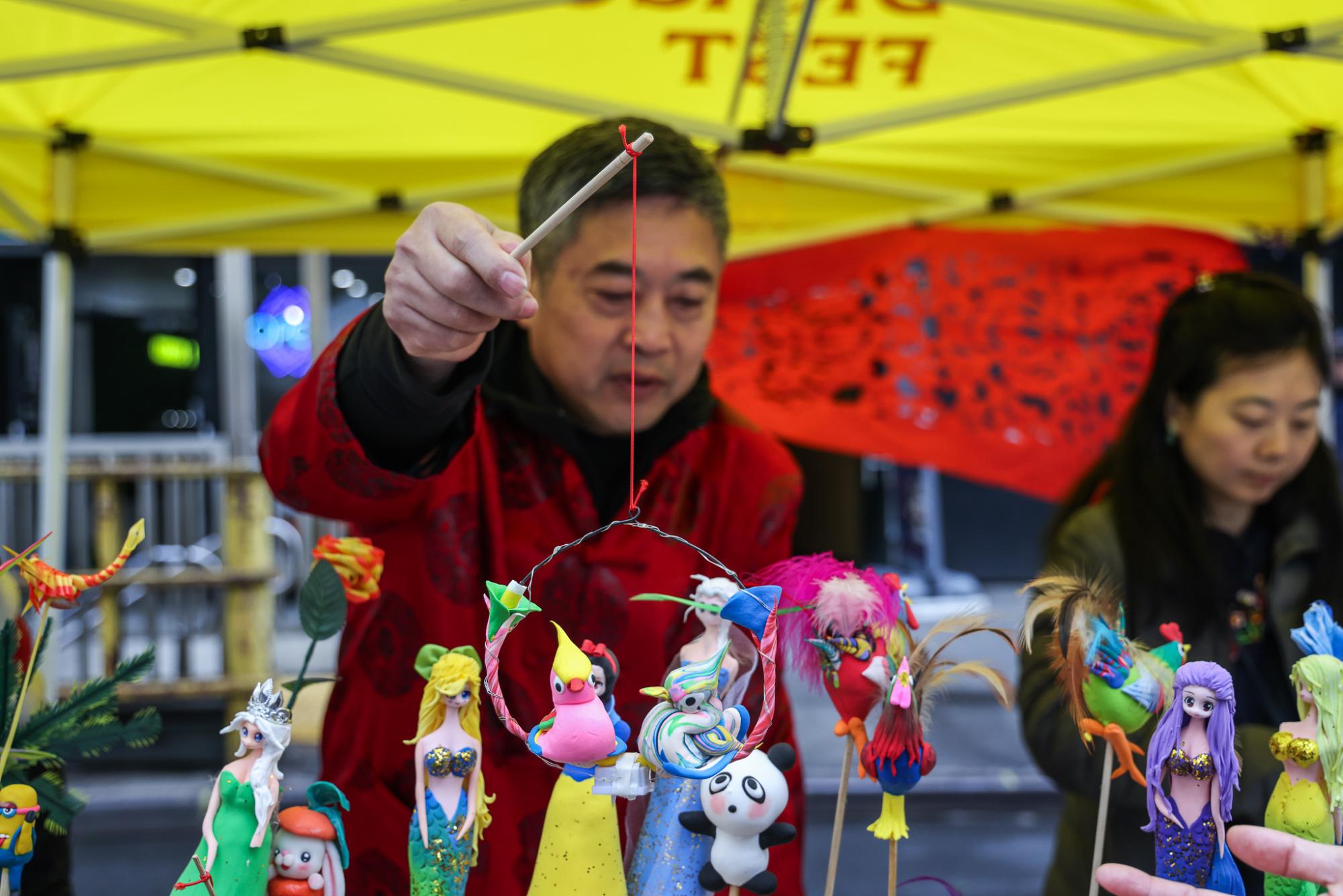 Man holds up dough bird figures attached to a red string and a stick with wire.