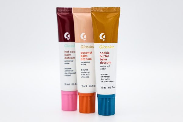 Three white lip gloss tubes labeled ‘BALMDOTCOM’ with colorful caps and labels in brown, pink, blue and red. 